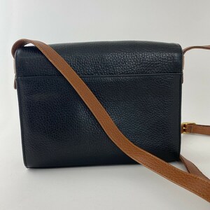 May include: A black leather crossbody bag with a brown leather strap. The bag has a flap closure and a small pocket on the back.