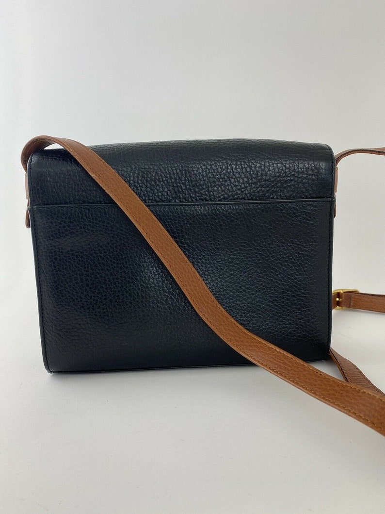 May include: A black leather crossbody bag with a brown leather strap. The bag has a flap closure and a small pocket on the back.
