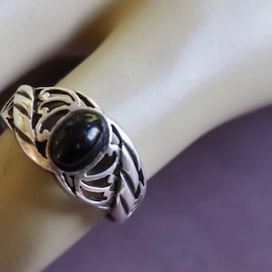 May include: A silver ring with an oval black stone set in a filigree design.