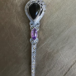 K&ouml;nnte beinhalten: Vintage Brosche in Silberoptik mit einem schwarzen Onyxstein und einem tropfenf&ouml;rmigen Amethysten. Die Brosche ist mit Markasitsteinen besetzt und hat eine lange, spitze Nadel.