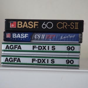 May include: A stack of four audio cassette tapes. The top tape is black with "BASF 60 CR-SII" printed on it. Below it is a blue tape with "BASF CS II" and "Fantastic Sound". The bottom two tapes are silver with "AGFA F-DXIS 90" printed on them.