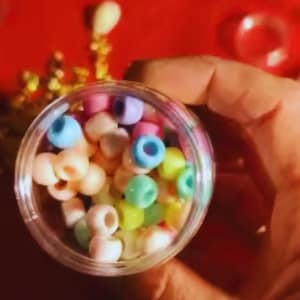 Pode incluir: Um recipiente de plástico transparente preenchido com uma coleção de pequenas contas redondas tipo pony em cores pastel. As contas apresentam um acabamento liso e um orifício central, exibindo uma variedade de tons suaves, incluindo azul claro, rosa, amarelo e verde.