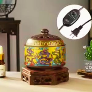 May include: A round ceramic electric incense burner with a yellow body featuring colourful dragon illustrations and a brown lid with cutouts. It sits on a dark brown carved wooden base and includes a black power cord with a temperature control dial.