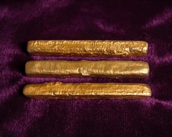 Puede incluir: Tres barras rectangulares de color dorado con una superficie texturizada e irregular. Cada barra tiene bordes redondeados y un acabado metálico, dispuestas horizontalmente en una pila paralela, mostrando un aspecto orgánico y rugoso.