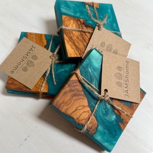May include: A set of square coasters with a teal resin and wood design. The coasters are tied together with twine and have a small tag that reads "JAMShome". The wood has a natural grain pattern.