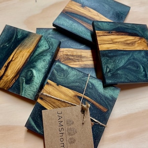May include: A set of square coasters with a unique design. Each coaster features a combination of dark teal resin and natural wood grain. The wood grain is a light brown color. The coasters are tied together with twine and a tag.