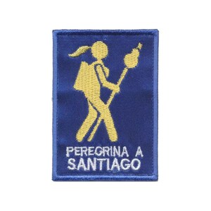 Op de afbeelding: Een rechthoekige blauwe geborduurde patch met een gele silhouet van een wandelaar met een rugzak en een staf met een schelpsymbool. De tekst PEREGRINA A SANTIAGO is in witte hoofdletters onderaan de patch geborduurd.