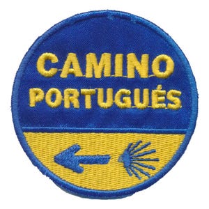 Op de afbeelding: Ronde geborduurde patch met de tekst "CAMINO PORTUGUÊS" in geel op een blauwe achtergrond. De onderste helft is geel, met een blauwe pijl en een gestileerd symbool.