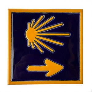 May include: Square ceramic tile with a navy blue background and a yellow sunburst design. A yellow arrow points right. The tile has a yellow border.