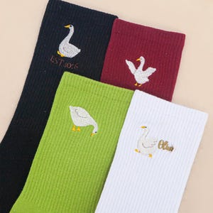 May include: Four ribbed socks in black, maroon, lime green, and white. Each sock features an embroidered white goose with an orange beak and feet. The black sock has the text EST 10:6 and the white sock has the text Olive embroidered in gold.