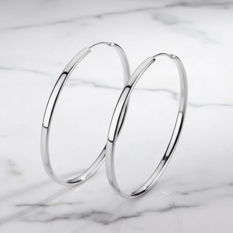 May include: A pair of large, polished silver-tone hoop earrings. These circular earrings feature a smooth, reflective metallic finish and a thin, lightweight construction. The design is simple and classic, consisting of two continuous metal loops.