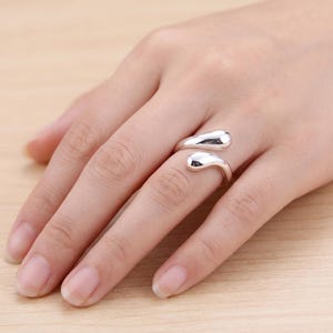 May include: A polished silver-tone open ring featuring two smooth, rounded, teardrop-shaped ends that curve towards each other. The metal has a reflective, high-gloss finish, creating a sleek and continuous appearance on the finger.