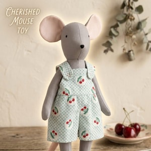 May include: A grey fabric mouse toy with large pink-lined ears, wearing light green overalls featuring a white polka dot pattern and a red cherry print. The text "CHERISHED MOUSE TOY" is visible in the upper left corner of the image.