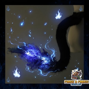 May include: A black faux fur tail accessory featuring a voluminous, translucent blue flame effect attached to the tip. The flame element displays layered, wispy textures in shades of deep and light blue, accented by small, glowing blue embers.