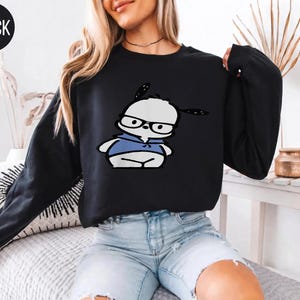 May include: A black long-sleeve sweatshirt featuring a graphic print of a white cartoon dog wearing black-rimmed glasses and a blue hooded sweatshirt. The text BLACK is printed in a small circle in the upper left corner of the image.