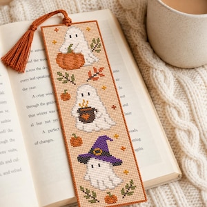 Peut inclure: Un marque-page rectangulaire en point de croix représentant trois fantômes blancs sur un tissu beige clair. Le fantôme du haut tient une citrouille orange, celui du milieu un chaudron marron et celui du bas porte un chapeau de sorcière violet.