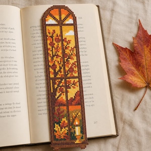 May include: A rectangular cross-stitch bookmark featuring an arched window design with a view of autumn trees in shades of orange, yellow, and brown. The scene includes a lit candle on a windowsill and white clouds visible through the window panes.