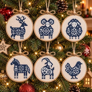 May include: Six circular wooden embroidery hoops containing white fabric with blue cross-stitched animal designs, including a deer, ram, sheep, horse, goat, and chicken. Each hoop features a jute twine hanger with a small wooden bead and bow.