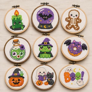 May include: Nine circular wooden embroidery hoops containing cross-stitch designs featuring Halloween themes including a green candle, a purple crystal ball with a bat, a gingerbread skeleton, a potion bottle, a frog in a witch hat, a bat-winged donut, a jack-o'-lantern, a ghost reading with a cat, and the text Boo.
