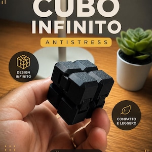Pode incluir: Um cubo infinito preto, segurado por uma mão, com o texto "CUBO INFINITO ANTISTRESS". O cubo é feito de pequenos blocos texturizados. O texto adicional inclui "DESIGN INFINITO", "COMPATTO E LEGGERO" e "FOCUS & RELAX". Uma pequena planta suculenta está no fundo.
