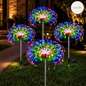 Op de afbeelding: Vier tuinlampen op zonne-energie met veelkleurige LED-vuurwerkeffecten op dunne zilveren metalen staven. Elke lamp heeft een ronde zonnepaneelvoet aan de onderkant van de staaf, met dunne draadjes die naar buiten uitsteken in een bolvorm.