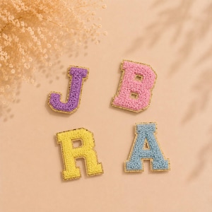 Può includere: Quattro toppe a forma di lettera in stile varsity con una superficie in ciniglia testurizzata e soffice, rifinite con un bordo glitterato dorato. Le lettere includono una J viola, una B rosa, una R gialla e una A azzurra per tessuti.