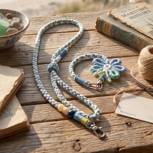 May include: A braided lanyard and a matching wristlet featuring light blue, white, and yellow cord with decorative beads and silver-toned metal lobster clasps. The wristlet includes a flower-shaped charm made of the same braided cord.