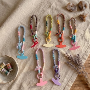 May include: Seven braided fabric lanyards with attached solid-colored T-shaped plastic clips. Each lanyard features a unique combination of multi-colored threads, small tassels, and a circular ring connecting the braided strap to the plastic clip.