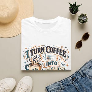 Könnte beinhalten: Ein weißes T-Shirt mit einem Grafikdruck, der den Text "I TURN COFFEE INTO" sowie eine Abbildung einer dampfenden Kaffeetasse, Programmierklammern und Computertastaturtasten mit der Aufschrift CTRL, ALT und dem Code-Symbol zeigt.