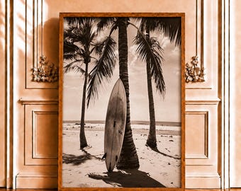 May include: A rectangular framed wall art piece featuring a black and white photograph of a surfboard leaning against a palm tree on a sandy beach. The scene includes ocean waves in the background and clear sky, all encased in a wooden frame.
