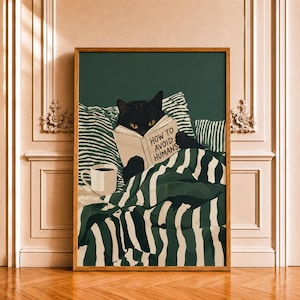 May include: A framed wall art print featuring a black cat with yellow eyes reading a book titled How to Avoid Humans whilst tucked under a green and white striped blanket with a white mug of coffee nearby on a dark green background.