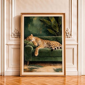 Peut inclure: Une impression d'art encadrée représentant un guépard aux taches noires dormant sur un canapé en velours vert foncé. Derrière le canapé se trouvent de grandes feuilles tropicales vertes sur un mur vert foncé. Le cadre est en bois clair.