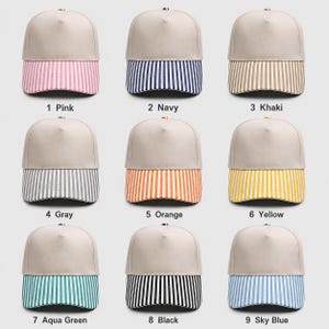 May include: Nine baseball caps arranged in a grid, each featuring a solid beige crown and a striped brim. The brims come in pink, navy, khaki, gray, orange, yellow, aqua green, black, and sky blue. Each cap is labeled with a number and color name.