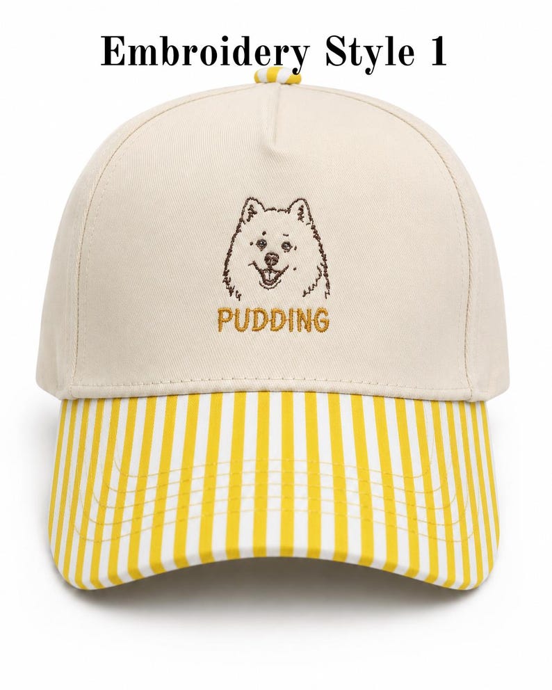 May include: A cream-colored baseball cap featuring a brown embroidered dog illustration above the text PUDDING in gold thread. The cap has a yellow and white vertical striped brim and a small yellow and white striped button on the top crown.