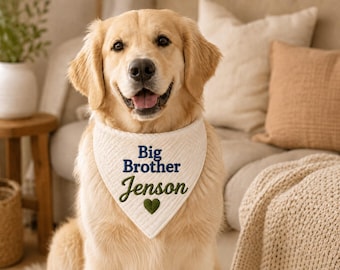 May include: A cream-colored, quilted dog bandana featuring the embroidered text "Big Brother" in dark blue, the name "Jenson" in green, and a small green heart icon centered below the name, worn by a golden retriever dog.