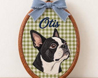 May include: An oval wooden embroidery hoop frame containing a green and white gingham fabric background. The fabric features an embroidered black and white Boston Terrier dog portrait and the name Otis in blue script, topped with a blue bow.