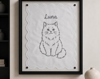 May include: A framed wall art piece featuring a white fabric panel with a scalloped edge and dark embroidery. The design includes a detailed line drawing of a fluffy cat centered below the embroidered name Luna in a cursive script font.