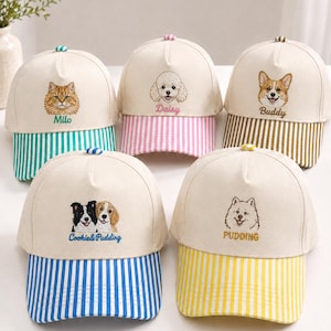Op de afbeelding: Vijf baseballpetten met off-white kronen en gestreepte kleppen. Elke pet heeft een geborduurd dierengezicht en een naam: Milo, Daisy, Buddy, Cookie & Pudding en Pudding. De kleppen zijn groen, roze, bruin, blauw en geel gestreept.