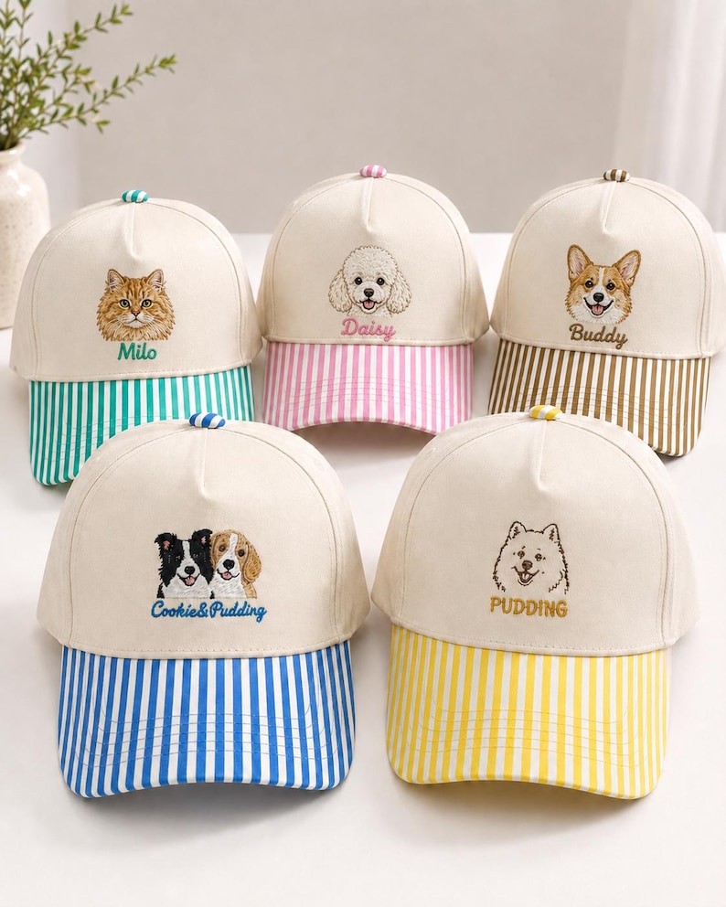 May include: Five off-white baseball caps with embroidered pet portraits and names. Each cap features a striped brim in green, pink, brown, blue, or yellow. The embroidery includes Milo, Daisy, Buddy, Cookie & Pudding, and Pudding with their names.