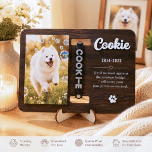 May include: A dark wood memorial plaque featuring a photo of a white dog, a black collar with rhinestone letters spelling COOKIE, and the text Cookie, 2014-2026, and a poem about the rainbow bridge with a white paw print icon.
