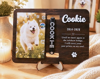May include: A dark wood memorial plaque featuring a photo of a white dog, a black collar with rhinestone letters spelling COOKIE, and the text Cookie, 2014-2026, and a poem about the rainbow bridge with a white paw print icon.