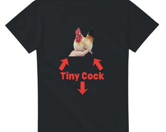 Pode incluir: T-shirt preto com um desenho de galo colorido e o texto "Tiny Cock" em vermelho. O galo está pousado numa mão, com setas vermelhas a apontar para o texto. Design humorístico.