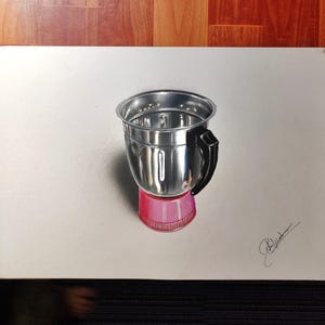 May include: A realistic drawing of a stainless steel blender jar with a black handle and a pink base. The metallic surface reflects light, showing highlights and shadows. A signature is visible in the bottom right corner of the white paper.