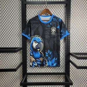 Könnte beinhalten: Ein kurzärmeliges T-Shirt mit Rundhalsausschnitt in Schwarz und Blau, das auf der Vorderseite eine große Grafik eines blauen Ara-Papageis zeigt. Das Shirt hat einen blauen Kragen und Ärmelabschlüsse sowie das CBF Brasil-Logo und fünf weiße Sterne.