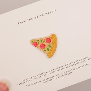 May include: An embroidered pizza slice patch with a golden crust, beige cheese, and pink pepperoni toppings. The patch is attached to a white card featuring the text from the patch haus and instructions for sewing the patch onto clothing.