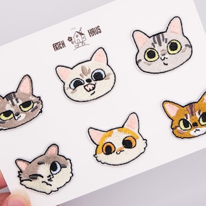 Pode incluir: Seis emblemas bordados de cabeças de gato dispostos num cartão branco com o texto THE PATCH HAUS. Os emblemas mostram vários rostos felinos com expressões, cores e padrões distintos, incluindo designs tigrados, tricolores e de cor sólida.