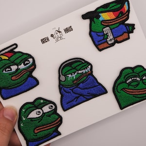 Könnte beinhalten: Fünf gestickte Aufnäher mit der grünen Froschfigur Pepe in verschiedenen Ausdrücken und Outfits, darunter einer mit Regenbogen-Sonnenbrille, einer mit Propellermütze, einer weinend in einer blauen Decke, einer schwitzend und einer lächelnd. Text: THE PATCH HAUS.