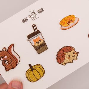 May include: A set of six embroidered patches on a white card featuring a brown squirrel, a coffee cup with a fox face, a yellow pumpkin, a slice of pie, a brown hedgehog, and an acorn. The text THE PATCH HAUS is printed at the top.