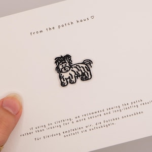May include: A small black and white embroidered dog patch centered on a white card. The card features the text from the patch haus with a heart symbol, and instructions in English and German regarding sewing the patch onto clothing items.