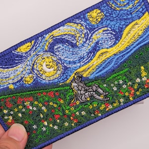 May include: A rectangular embroidered patch featuring a night sky with swirling blue and yellow patterns above a green field filled with colorful flowers. A small, grey armored figure sits in the center of the field, surrounded by red and white blossoms.
